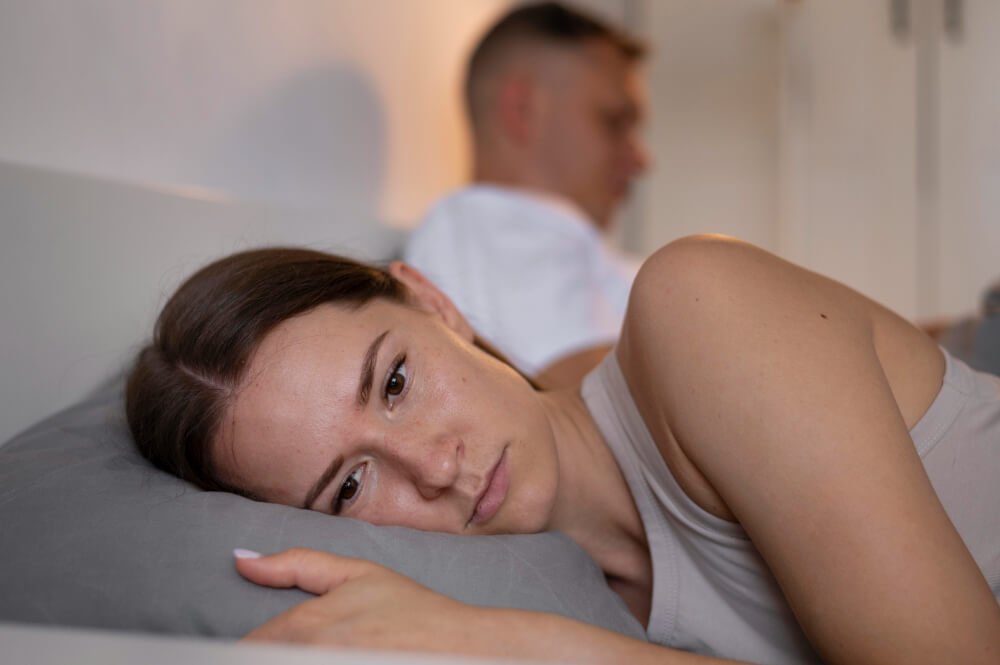 Couple au lit se tournant le dos, illustrant la distance émotionnelle et sexuelle causée par le reproche du manque d'initiative