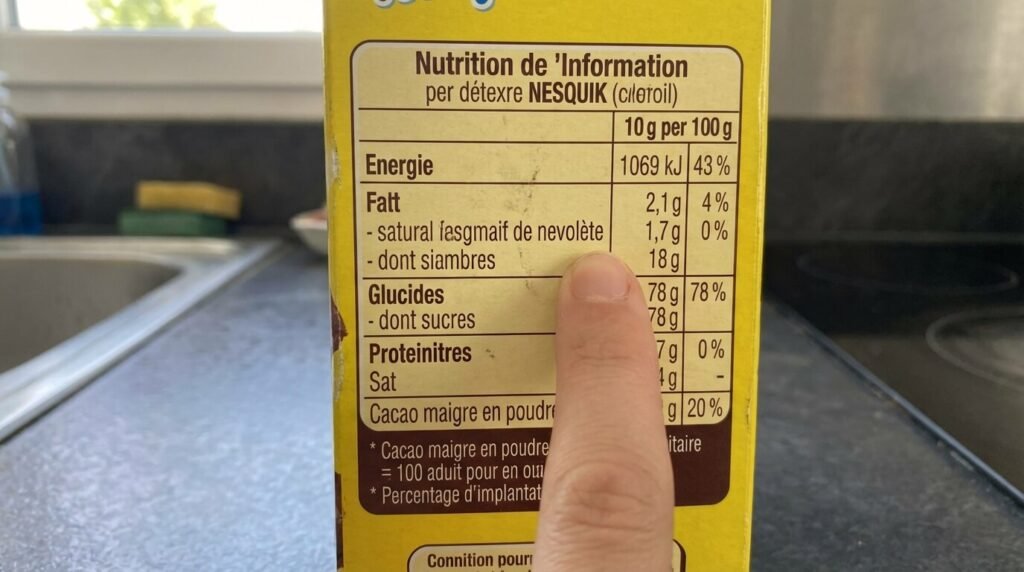 Zoom sur l'étiquette nutritionnelle d'une boîte de Nesquik montrant la teneur très élevée en sucre rapide par rapport au cacao
