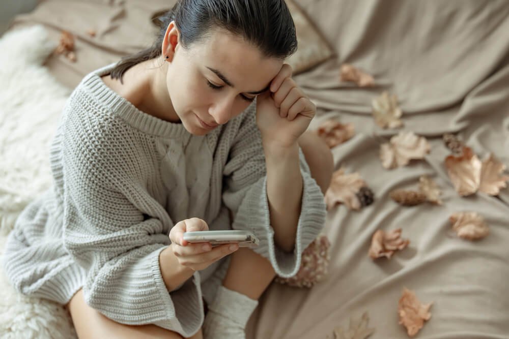 Femme pensive regardant son téléphone, tiraillée par la nostalgie des retrouvailles avec son amour de jeunesse