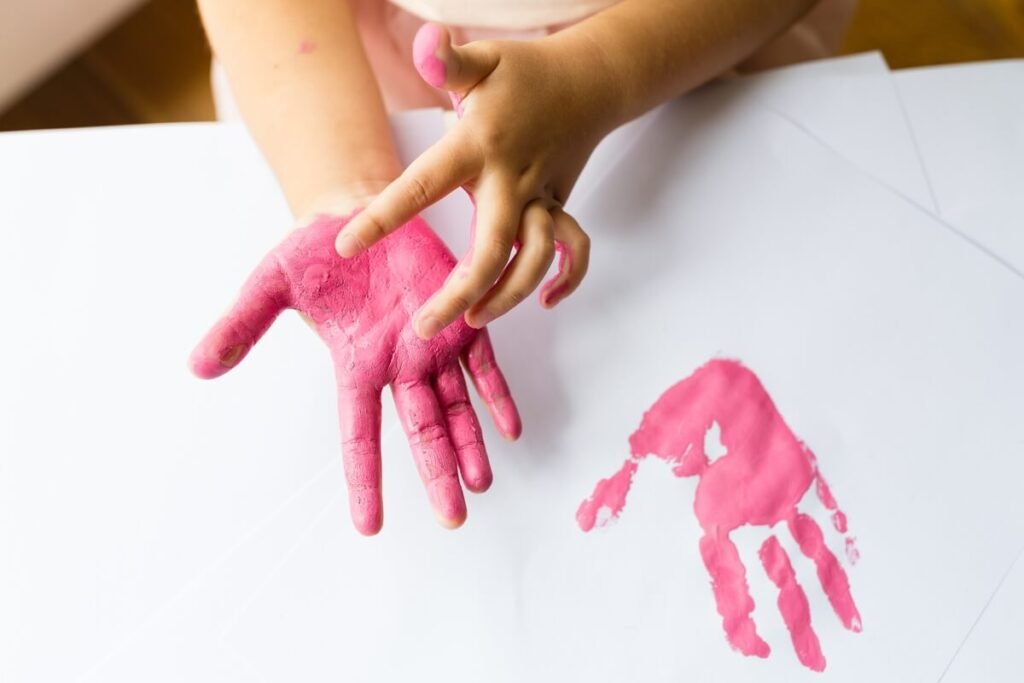 Quelle peinture pour empreinte bebe choisir sans danger ? 2 Main d'un nourrisson enduite de peinture rose lavable pour réaliser une empreinte sur toile.