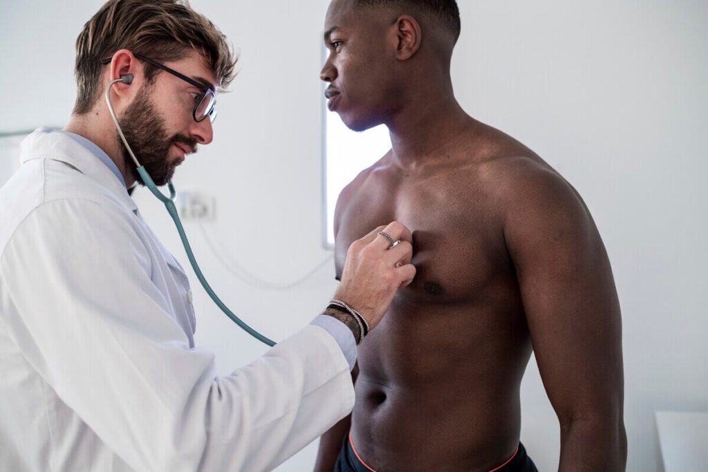 Bouton blanc sur le téton chez l'homme : quelles sont les causes et que faire ? 2 Médecin dermatologue examinant la peau du buste d'un patient masculin