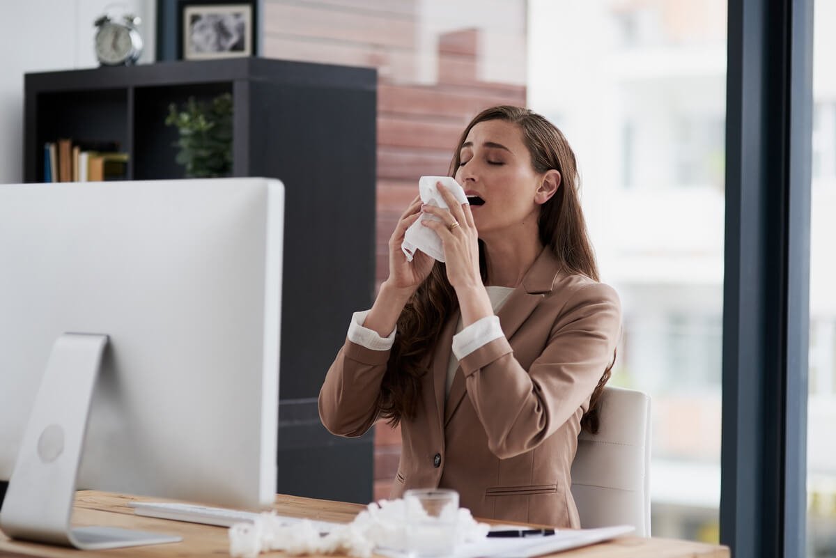 Femme toussant dans son bureau à cause de l'air conditionné soufflant au-dessus d'elle