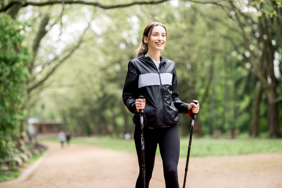 Femme souriante pratiquant la marche active en forêt avec des vêtements de sport