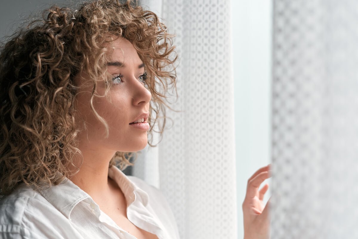 Femme au regard apaisé regardant par la fenêtre, illustrant l'absence de manque émotionnel