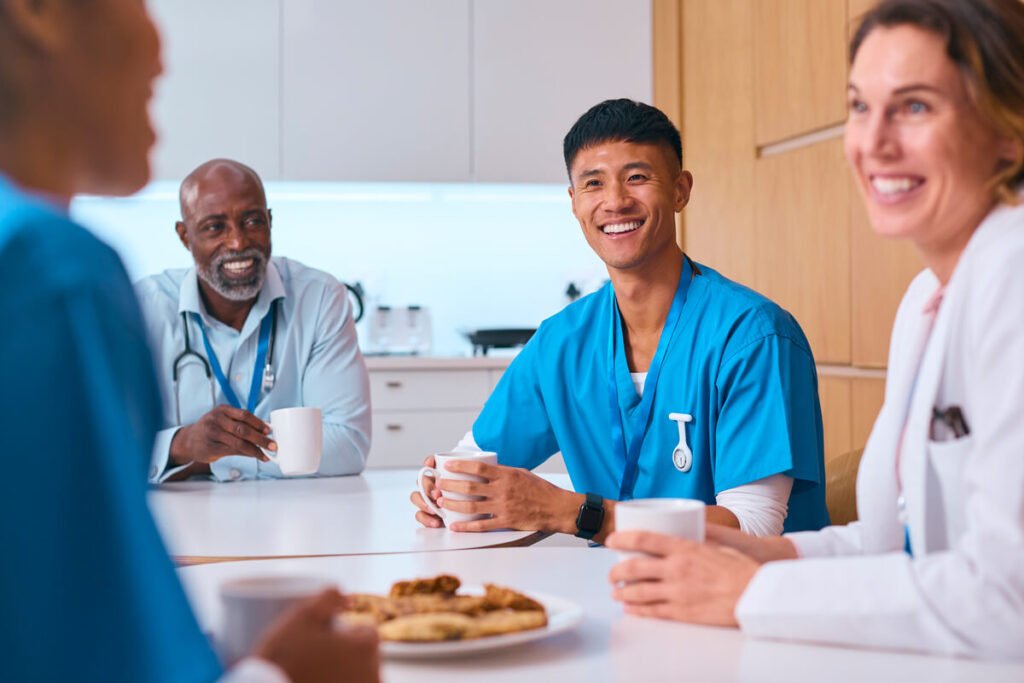 Quoi offrir à une équipe médicale pour marquer le coup ? 3 Personnel médical souriant partageant une pause café dans une salle de repos de clinique.