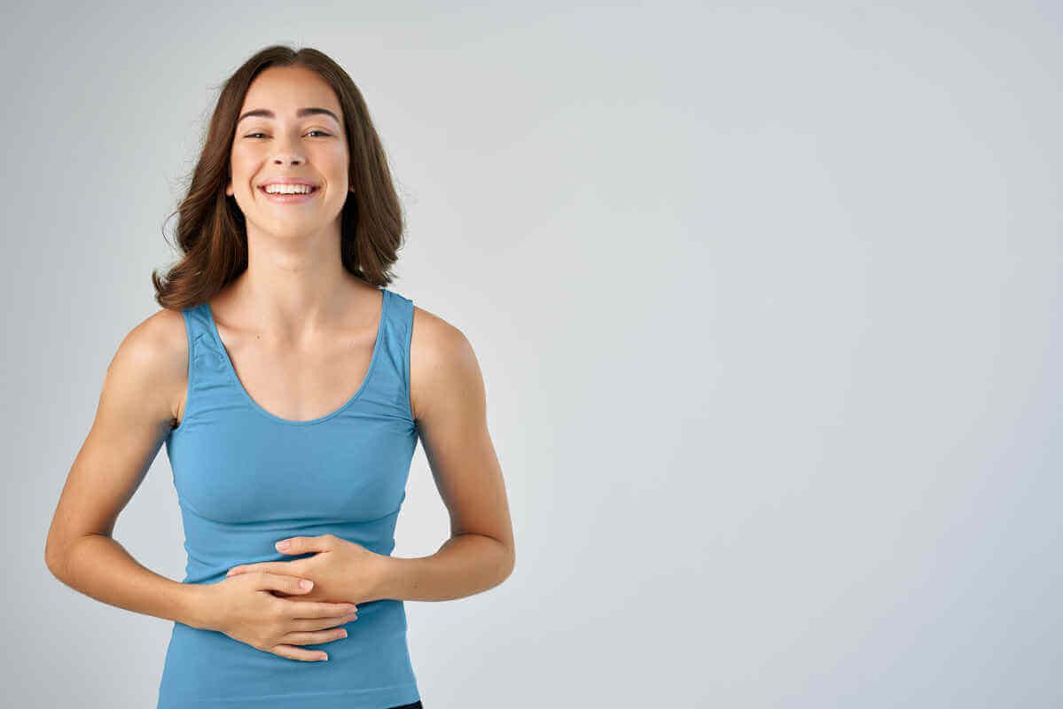 Une jeune femme pensive et souriante posant délicatement ses mains sur son ventre au réveil.