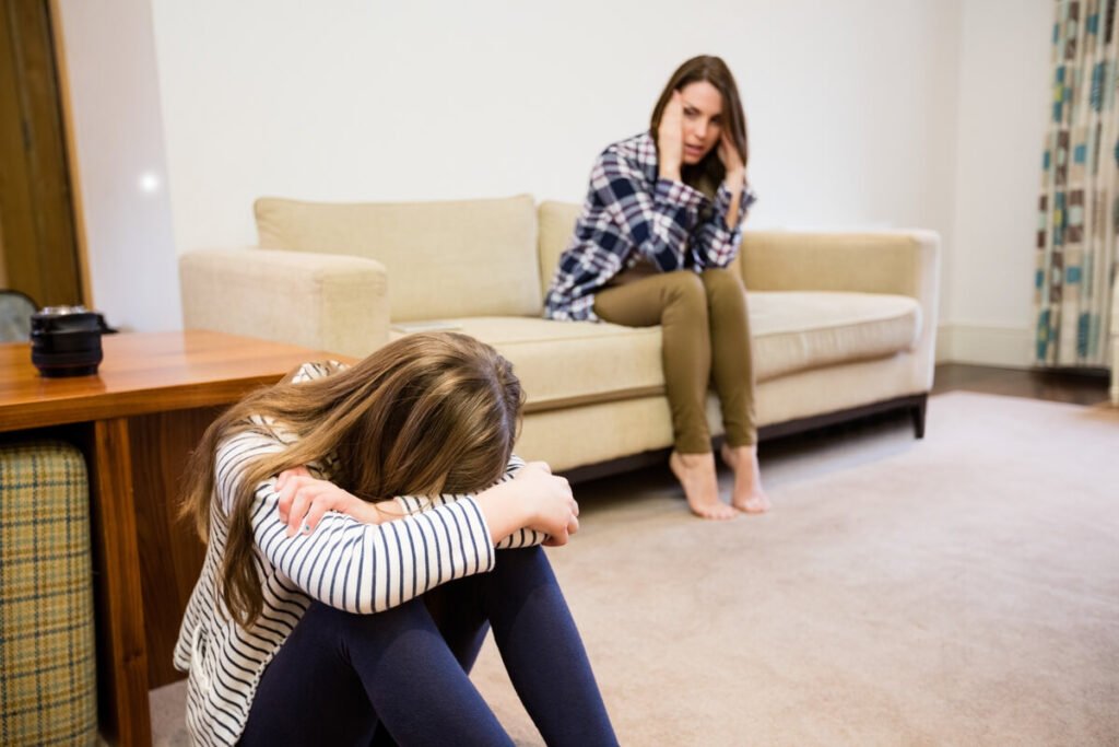 Une mère pensive et son adolescent assis dos à dos dans le salon après une dispute familiale.