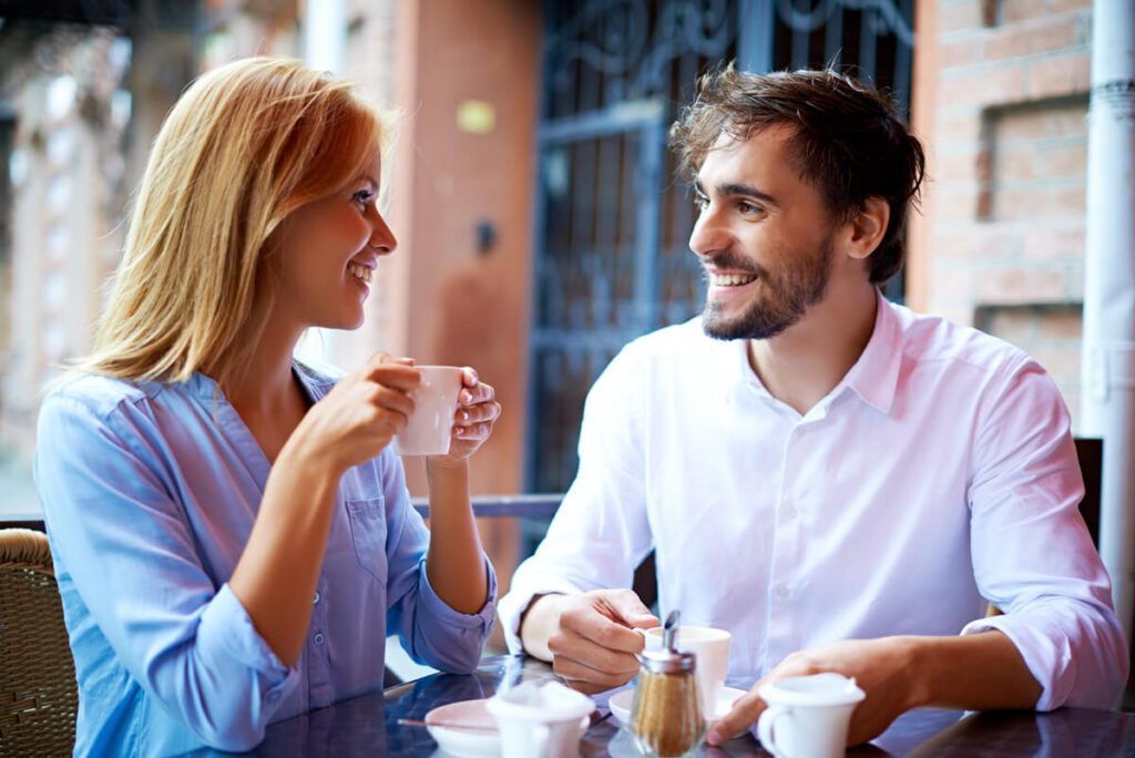 Est-il intéressé ou juste gentil ? Les vrais signes qui ne trompent pas 2 Un homme et une femme discutant joyeusement à la terrasse d'un café, se regardant dans les yeux.