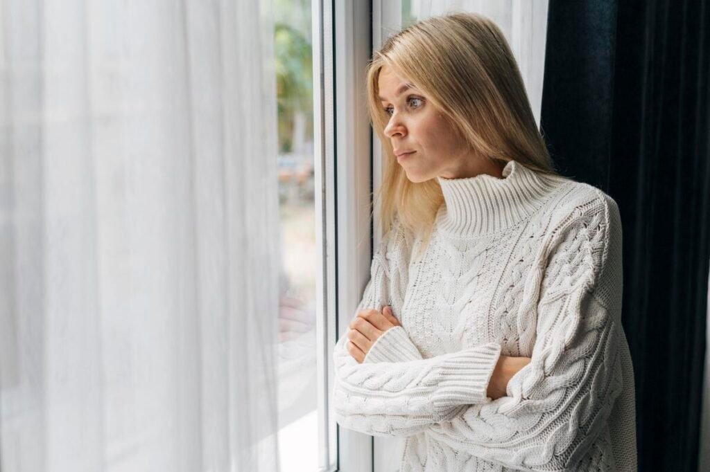 Une mère pensive regardant tristement par la fenêtre, exprimant la solitude.