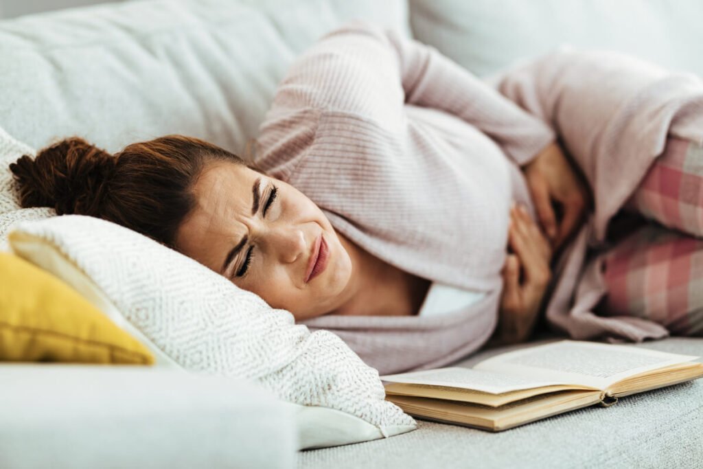 Personne assise sur son lit se tenant le ventre en raison de douleurs abdominales matinales.