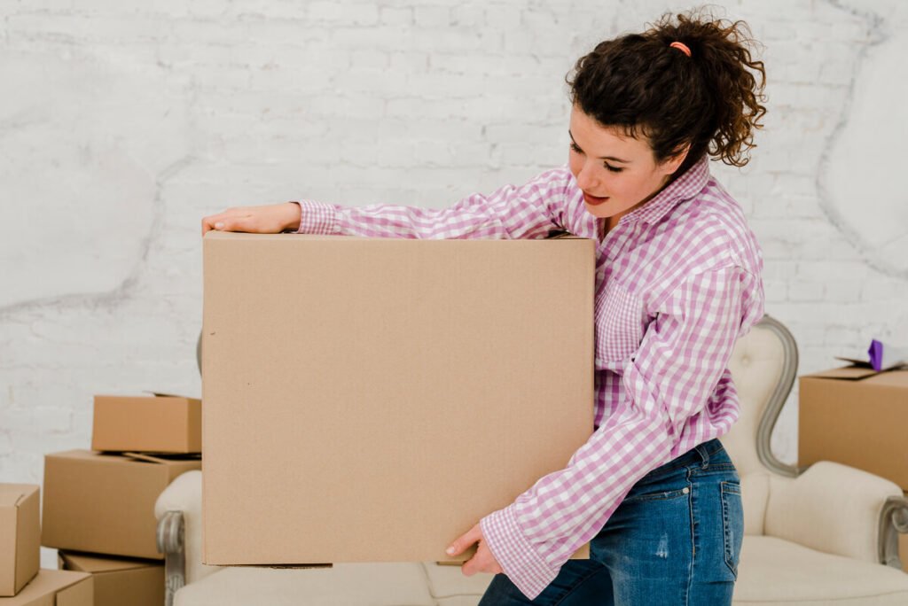 Jeune femme enceinte de quelques semaines soulevant un carton avec précaution lors d'un déménagement.