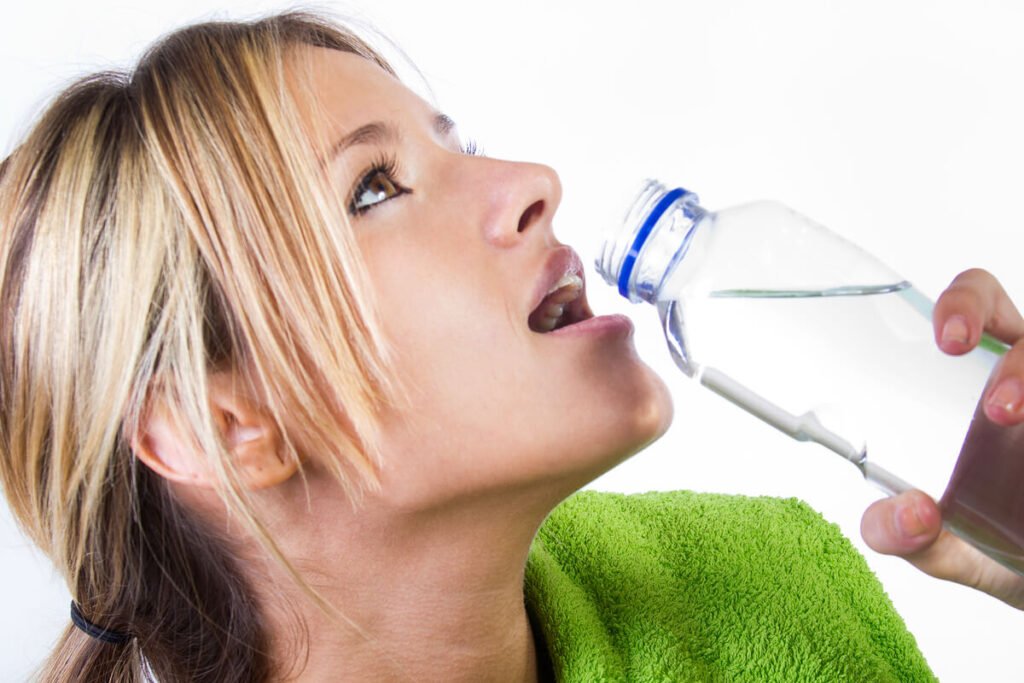 Personne buvant une grande bouteille d'eau tout en observant un gonflement œdémateux à ses chevilles.