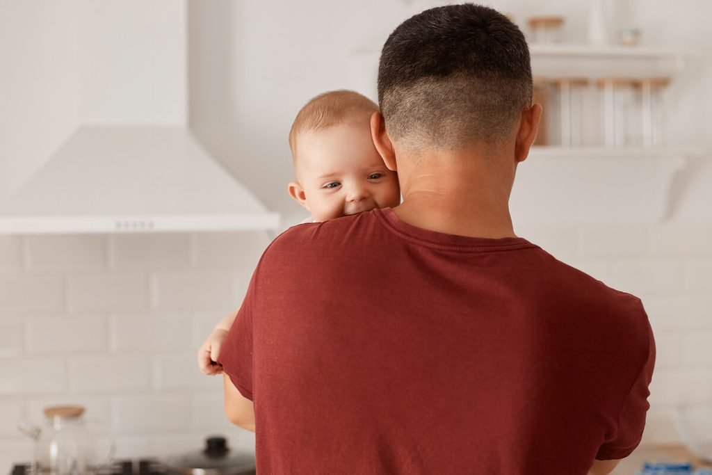 Bébé régurgite et redemande à manger : est-ce normal 3 Parent maintenant son bébé à la verticale contre son épaule après la tétée pour faciliter le rot.