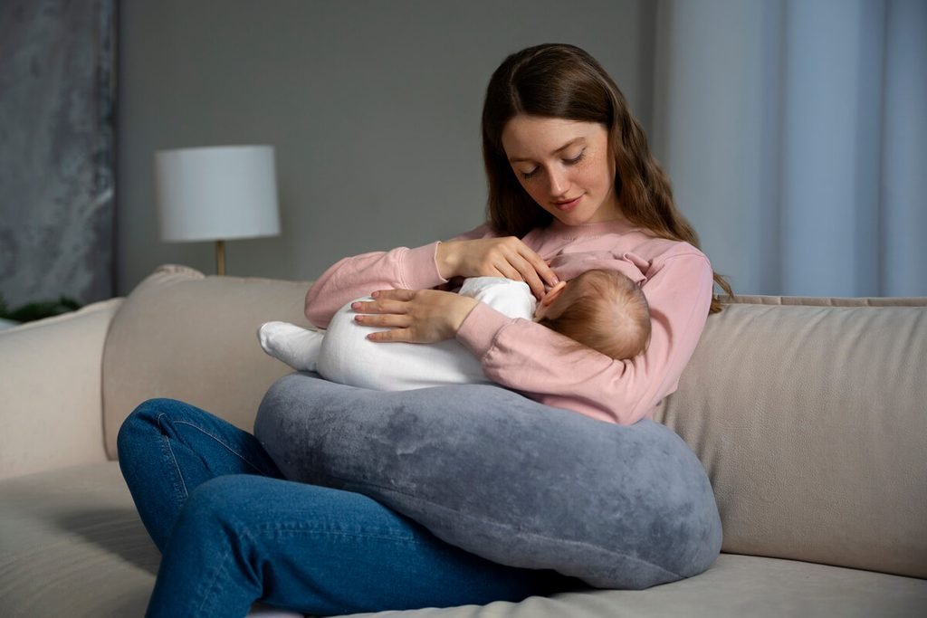 Comment soulager les douleurs de dos pendant la grossesse et les tétées ? 4 Jeune mère assise avec le dos bien calé et un coussin d'allaitement soutenant le nourrisson à hauteur de poitrine.