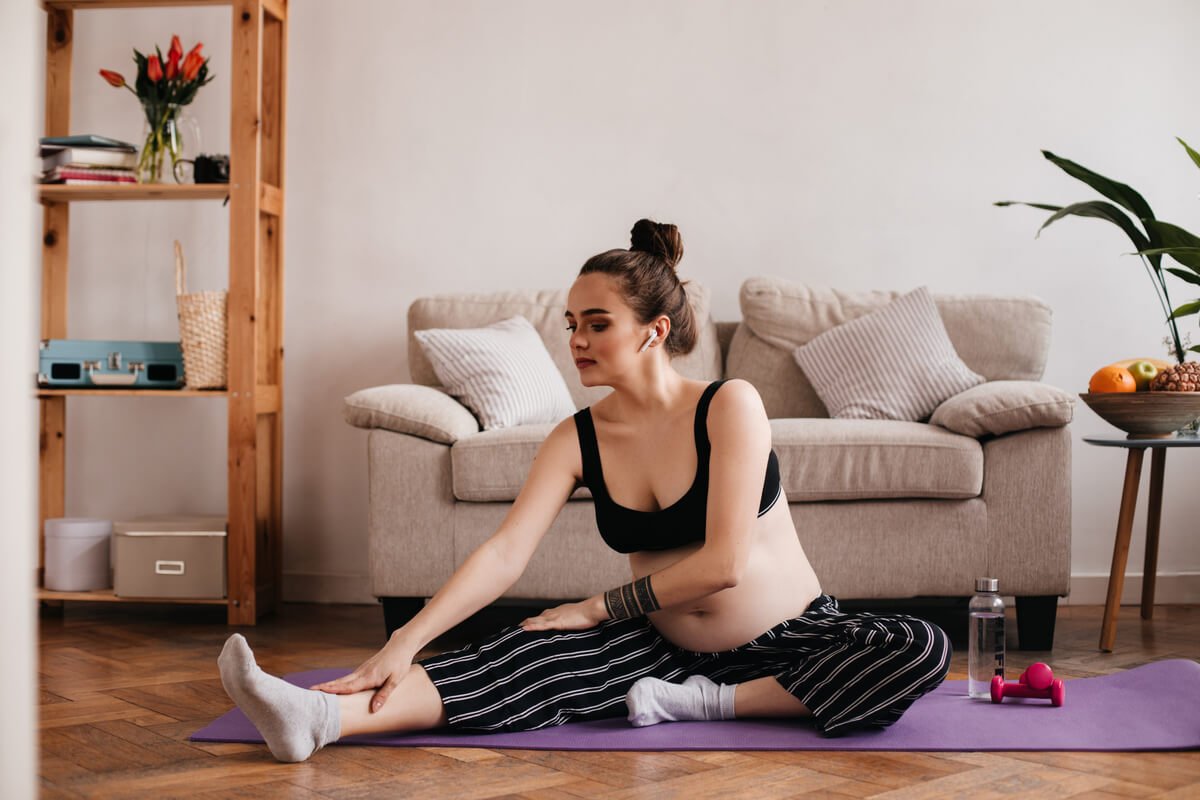Jeune maman réalisant des étirements et des exercices de respiration sur un tapis de fitness chez elle.