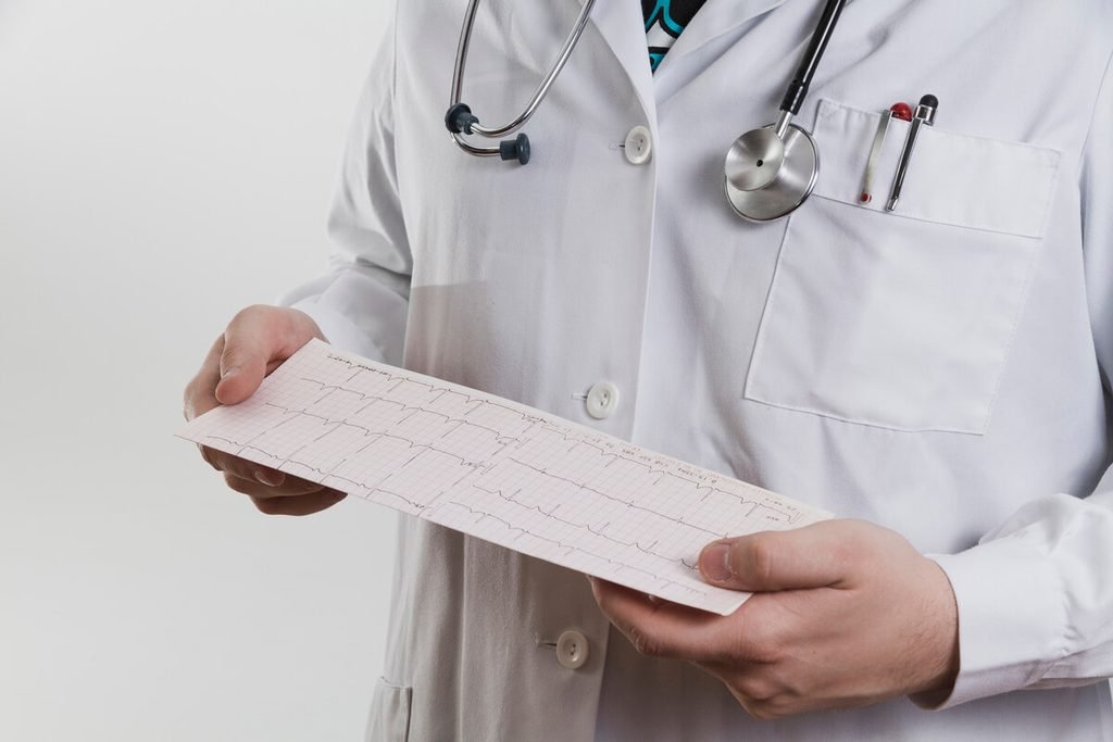 Palpitations, essoufflement, douleur thoracique : quand passer un électrocardiogramme ? 4 Médecin analysant les ondes et le rythme cardiaque sur le papier millimétré imprimé par l'électrocardiographe.