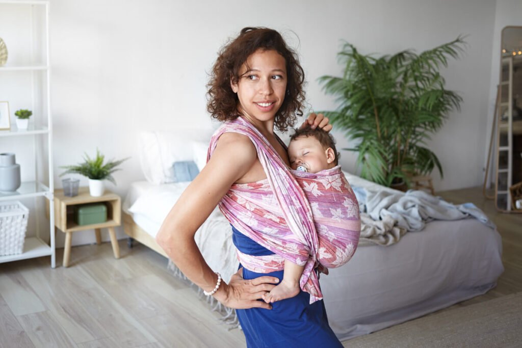 Mère vaquant à ses occupations avec son bébé blotti contre sa poitrine en écharpe de portage.