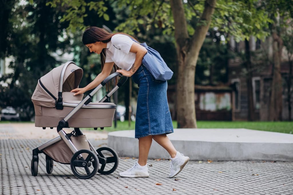 Mère pratiquant la marche sportive en extérieur dans un parc en poussant la poussette de son bébé.