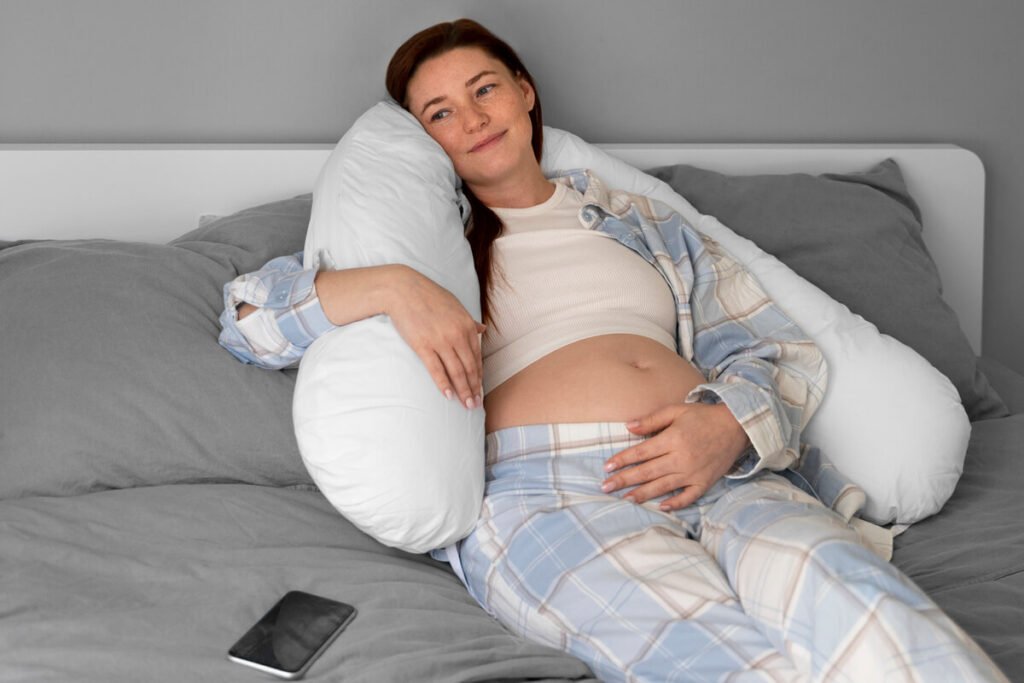 Comment soulager les douleurs de dos pendant la grossesse et les tétées ? 2 Femme enceinte allongée confortablement sur le côté avec un coussin de positionnement pour soulager les tensions du bas du dos.